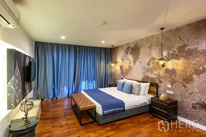 Condominium for rent in Pathum Wan, Bangkok - Bedroom with textured world-map accent wall, pendant lights, and blue bedding.