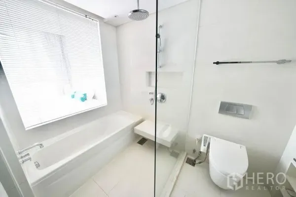 公寓 出租或出售在Watthana, Bangkok - 明亮的白色浴室，带浴缸、玻璃隔断雨淋花洒和壁挂式马桶。