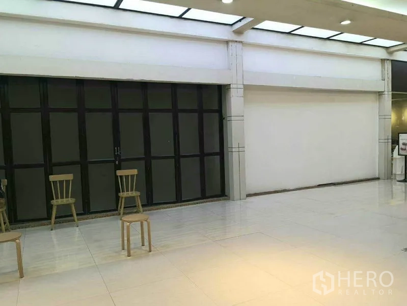 零售空间 出租在Khlong Toei, Bangkok - 玻璃店面朝向明亮的商场走廊，瓷砖地面与天窗。