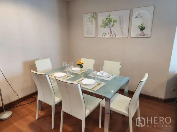 Condominium for rent in Huai Khwang, Bangkok - Bright dining corner featuring a glass-top table with six white chairs and wall art.