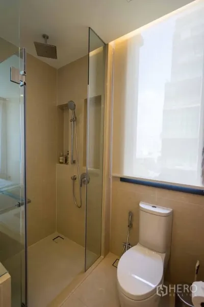 Condominium for rent in Watthana, Bangkok - Modern bathroom with glass-enclosed rain shower, toilet and large window.