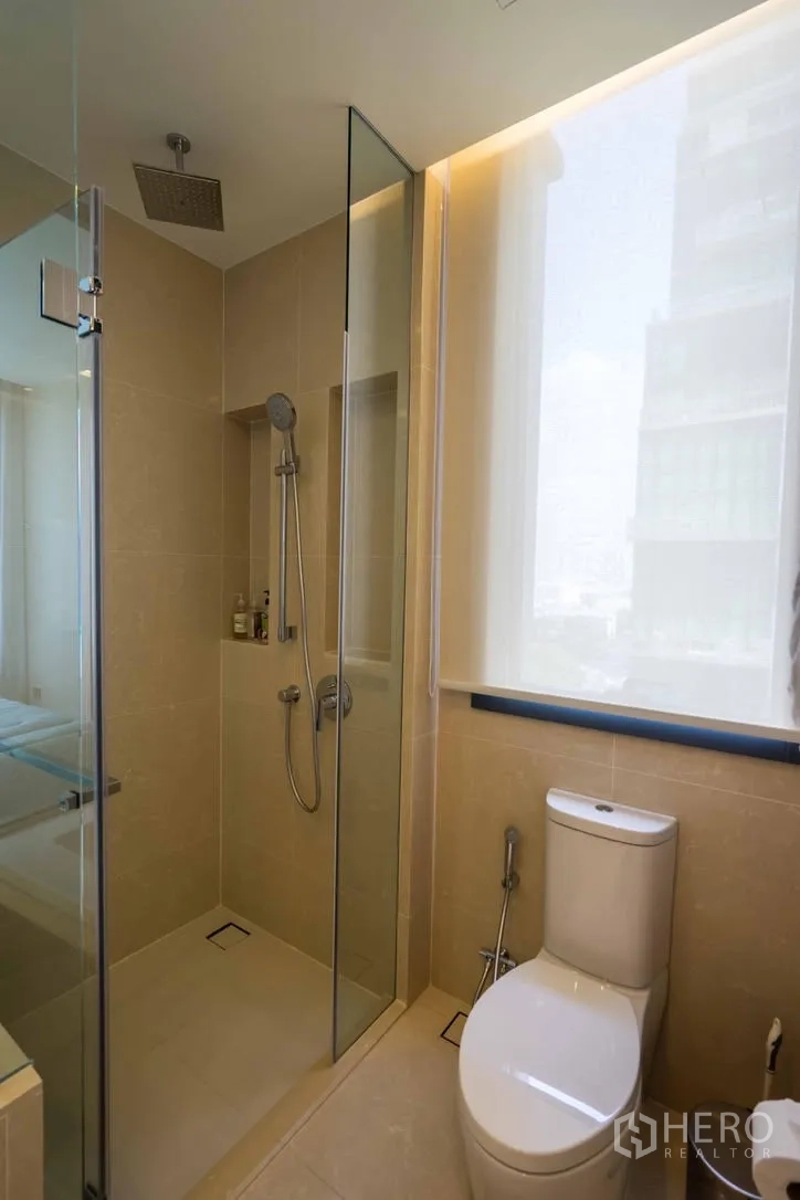 Condominium for rent in Watthana, Bangkok - Modern bathroom with glass-enclosed rain shower, toilet and large window.
