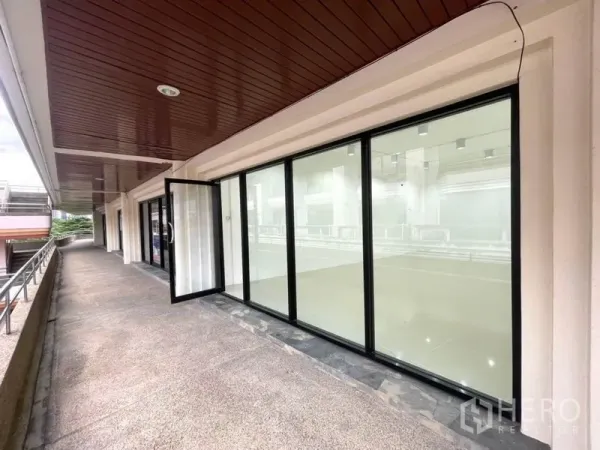 Office Space for rent in Khlong Toei, Bangkok - Covered outdoor walkway in front of the unit with long glass façade and railing.