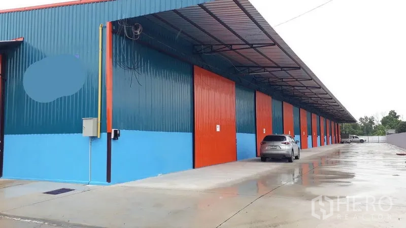 工厂 出租在Khlong Luang, Pathum Thani - 一排现代钢结构工厂单元，红色滑门，带顶装卸区与宽阔混凝土通道，位于空銮。