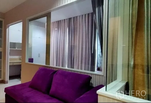 คอนโด ให้เช่าในPhaya Thai, Bangkok - พื้นที่นั่งเล่นโซฟาสีม่วง มีฉากกั้นกระจกมองเห็นห้องนอนและผ้าม่าน