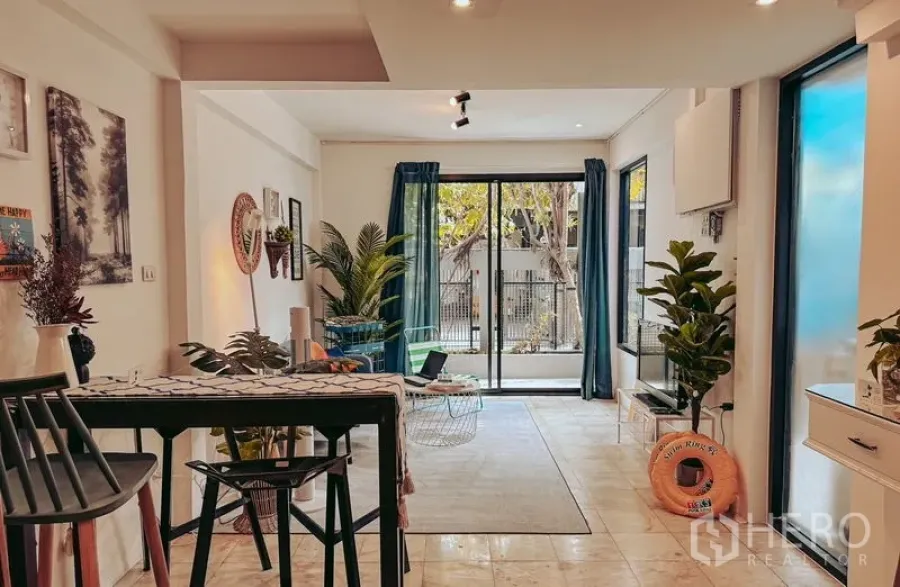 Home Office for rent in Watthana, Bangkok - Bright open-plan living area with sliding glass doors, blue curtains, and indoor plants.