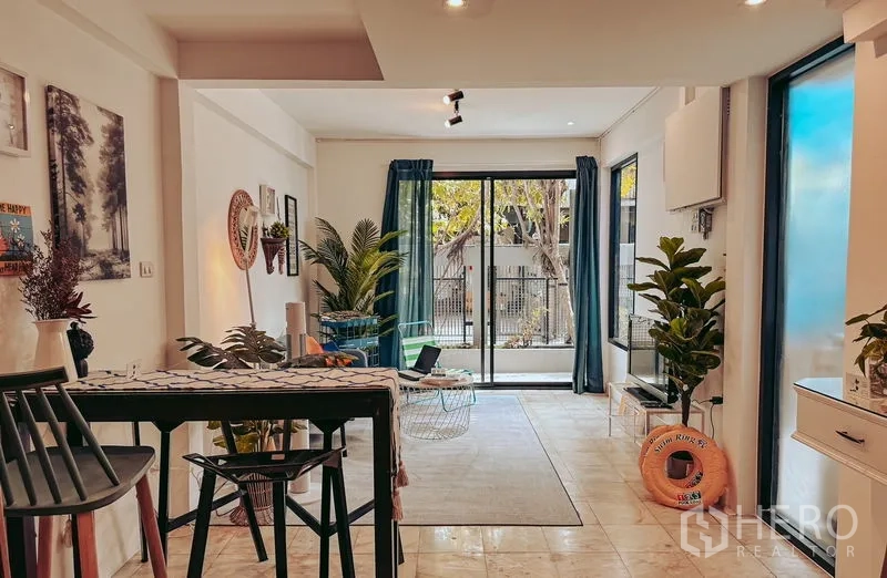 Home Office for rent in Watthana, Bangkok - Bright open-plan living area with sliding glass doors, blue curtains, and indoor plants.