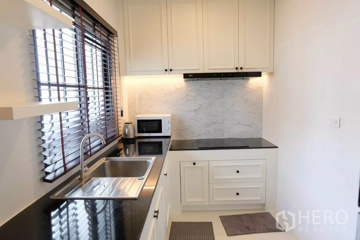 Detached House for sale in Bang Phli, Samut Prakan - Separate Thai kitchen with black countertops, sink, cooktop, range hood, microwave and window blinds