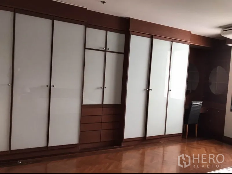 Condominium for rent or sale in Watthana, Bangkok - Bedroom with a wall of built-in wardrobes and a work desk.