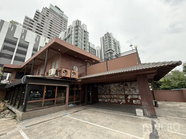 独立式住宅 出租在Watthana, Bangkok - 两层木质风格独栋建筑，前方宽阔停车区，背景为高层公寓，近Ekkamai