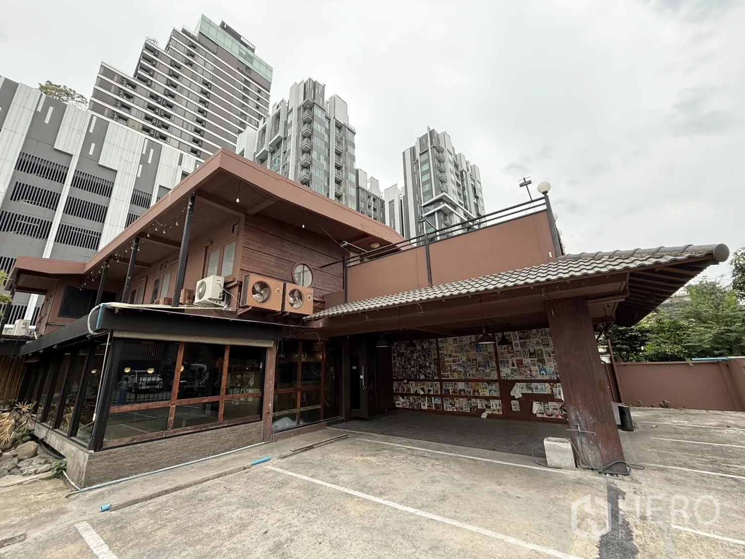 独立式住宅 出租在Watthana, Bangkok - 两层木质风格独栋建筑，前方宽阔停车区，背景为高层公寓，近Ekkamai