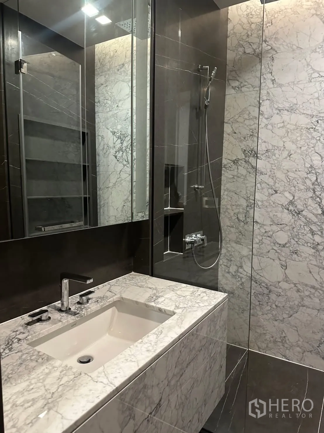 Condominium for rent or sale in Watthana, Bangkok - Marble-clad bathroom with vanity, mirror, and glass shower.