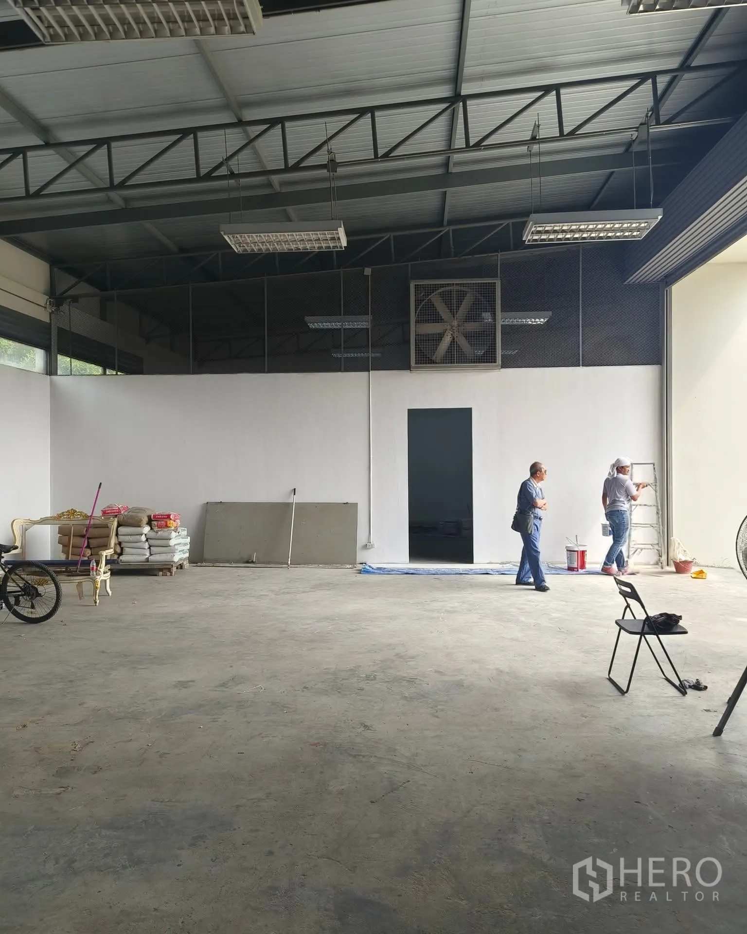 Warehouse for rent in Sai Mai, Bangkok - Open-plan storage area with a large ventilation fan, even concrete floor and a wide doorway for loading.