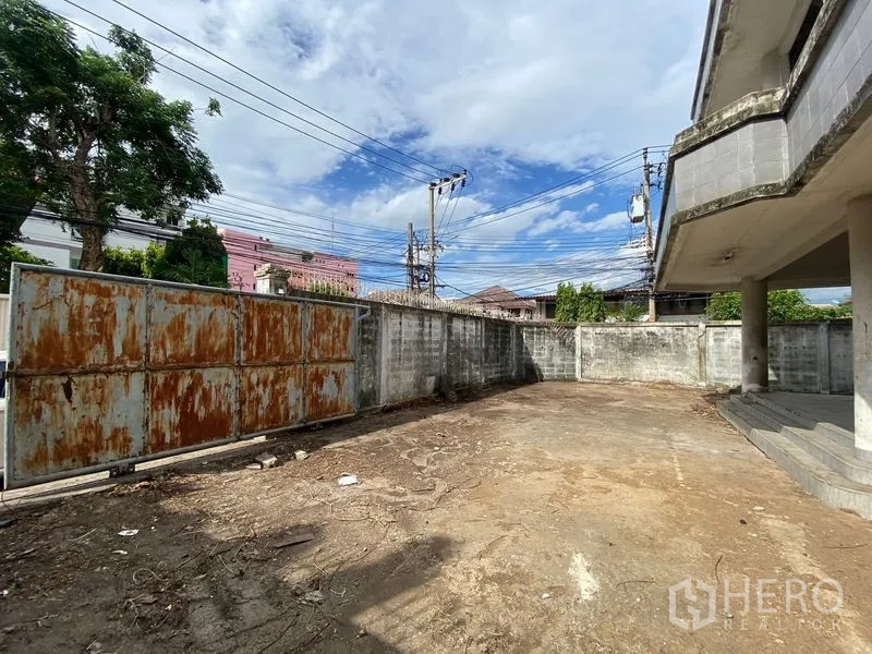 Office Space for sale in Wang Thonglang, Bangkok - Gated yard with a rusted sliding gate and perimeter wall providing secure parking.