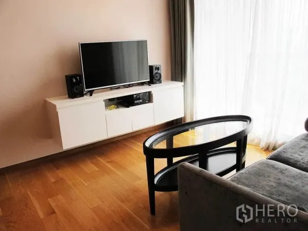 คอนโด ให้เช่าในWatthana, Bangkok - ห้องนั่งเล่นสว่าง ตู้ทีวีลอยตัว โทรทัศน์ ลำโพง โต๊ะกลางกระจกทรงวงรี และหน้าต่างบานใหญ่