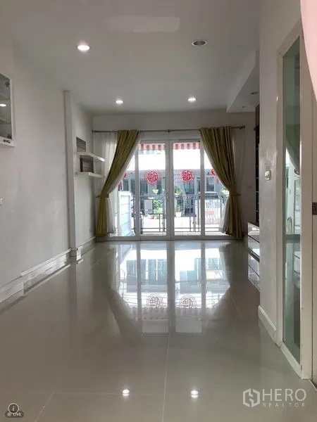 联排别墅 出租或出售在Wang Thonglang, Bangkok - 采光充足的客厅，亮面瓷砖地、筒灯与推拉落地门，绿色窗帘通向小露台。