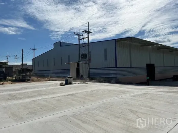 货栈 出租在Nikhom Phatthana, Rayong - 金属外墙仓库外观，宽阔混凝土硬地与电力设施，蓝天下（尼空帕他那）。