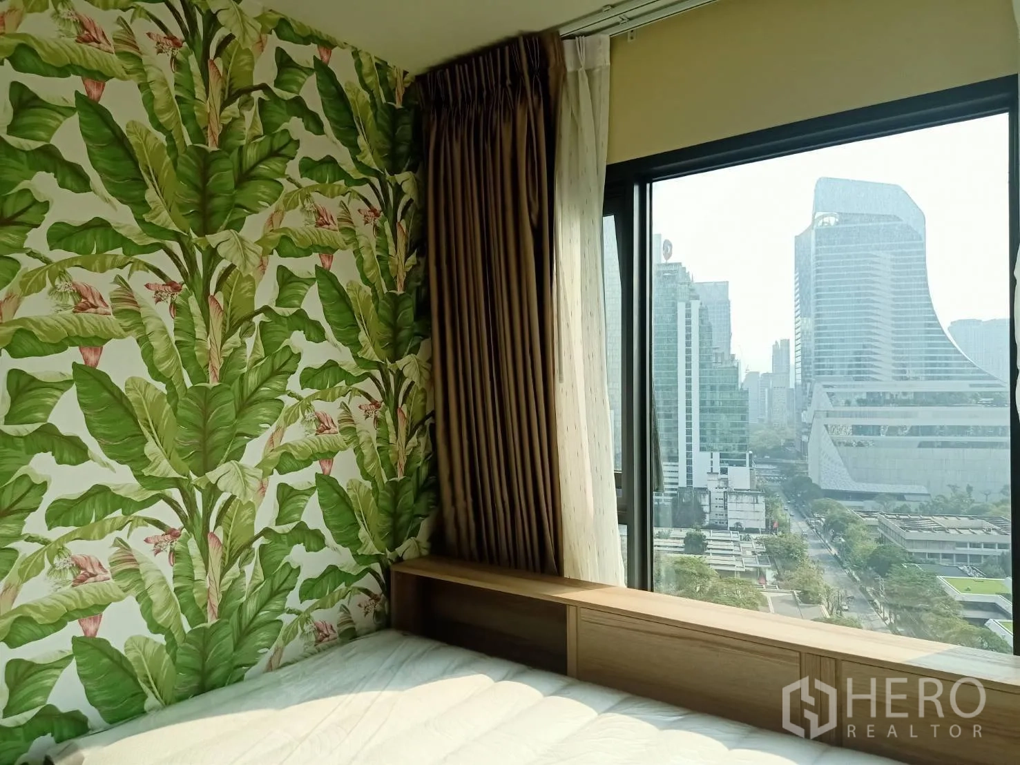 公寓 for rent in Pathum Wan, Bangkok - 卧室设热带叶子主题墙纸与宽窗，欣赏城市景观。