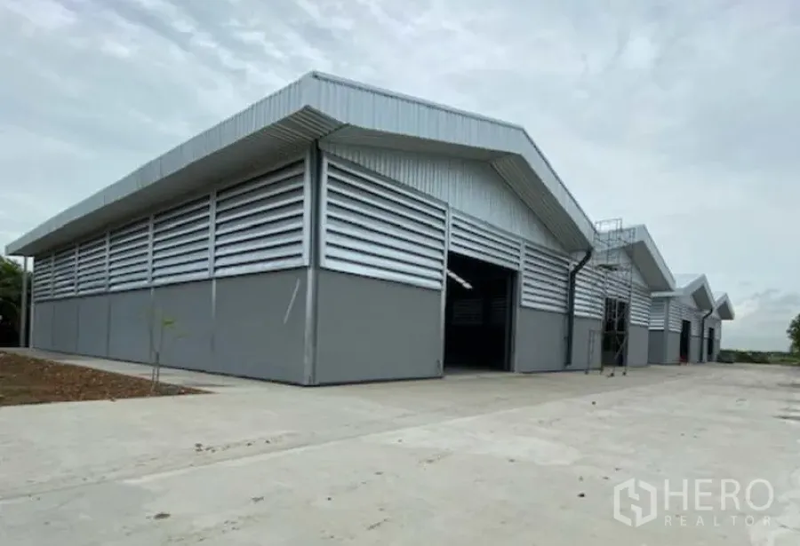 Factory for rent in Pathum Thani - Modern grey steel factory buildings with gable roofs, louvered walls and a wide concrete loading yard in Lat Lum Kaeo, Pathum Thani.