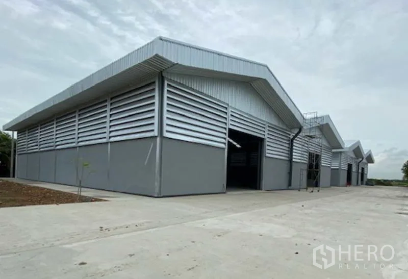 Factory for rent in Pathum Thani - Modern grey steel factory buildings with gable roofs, louvered walls and a wide concrete loading yard in Lat Lum Kaeo, Pathum Thani.