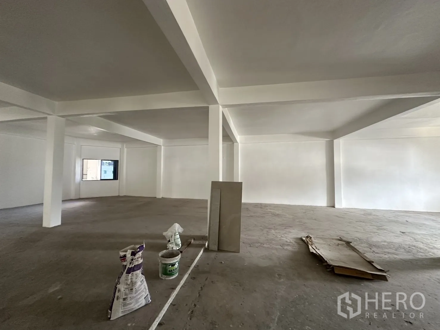 零售空间 for rent in Watthana, Bangkok - 宽敞未完成的零售室内，支撑立柱、混凝土地面和一扇窗户。
