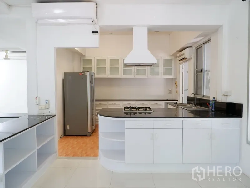 Detached House for rent in Khlong Toei, Bangkok - Main kitchen with island cooktop, range hood and glass-front cabinets.