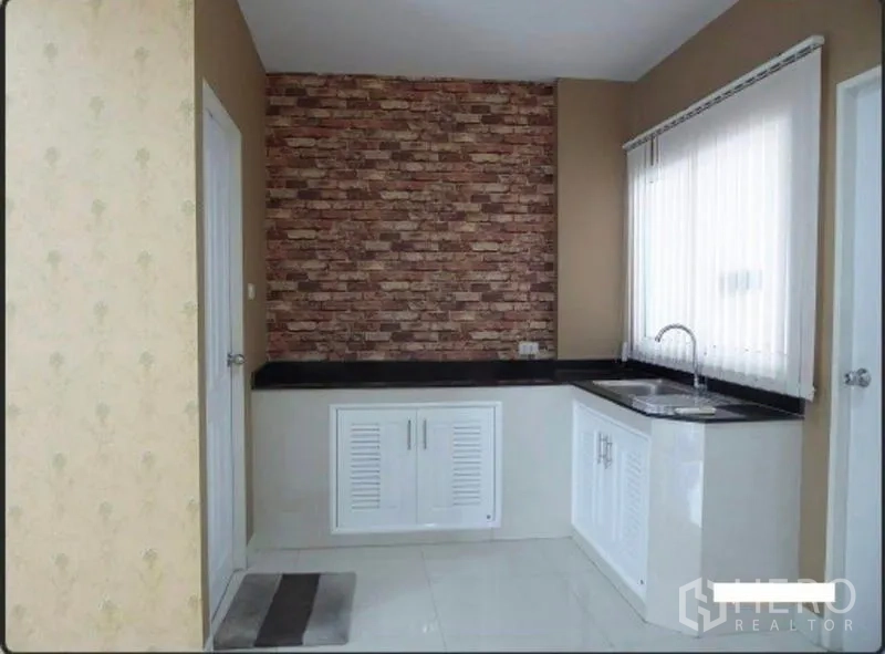 Home Office for rent in Bueng Kum, Bangkok - Compact pantry kitchen with white cabinets, black countertop, brick feature wall and corner sink.