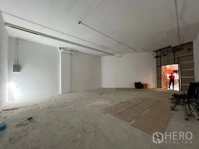 พื้นที่ขายปลีก ให้เช่า - พื้นที่ค้าปลีกแบบเปิดโล่ง พื้นคอนกรีต ผนังสีขาว และทางเข้าแบบบานม้วน พร้อมตกแต่ง