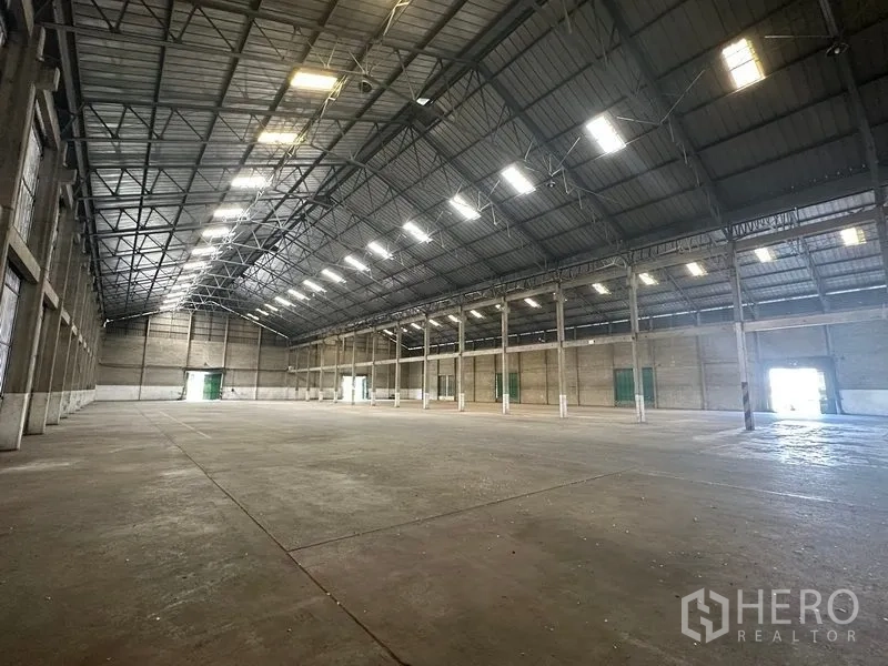 货栈 出租在Mueang Pathum Thani, Pathum Thani - 大型仓库分区，多个绿色推拉装卸门，车辆可穿行。
