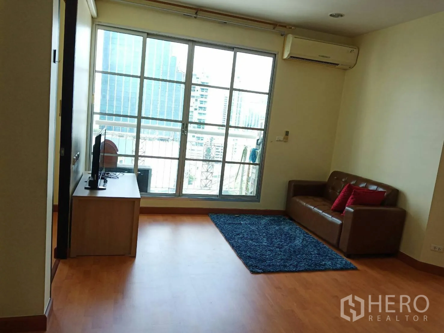 คอนโด ให้เช่าในKhlong Toei, Bangkok - ห้องนั่งเล่นสว่างไสว ประตูกระจกบานเลื่อนออกสู่ระเบียง เห็นวิวเมือง พร้อมชั้นวางทีวีและเครื่องปรับอากาศ