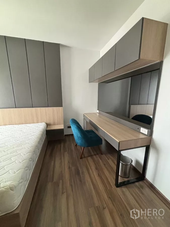 Condominium for rent or sale in Watthana, Bangkok - Bedroom with upholstered headboard, long work desk and overhead cabinets.