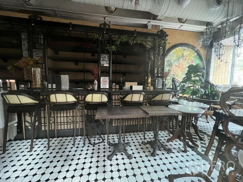 零售空间 出租在Watthana, Bangkok - 吧台全景，藤编吧椅、桌子及热带壁画与外露管线天花。