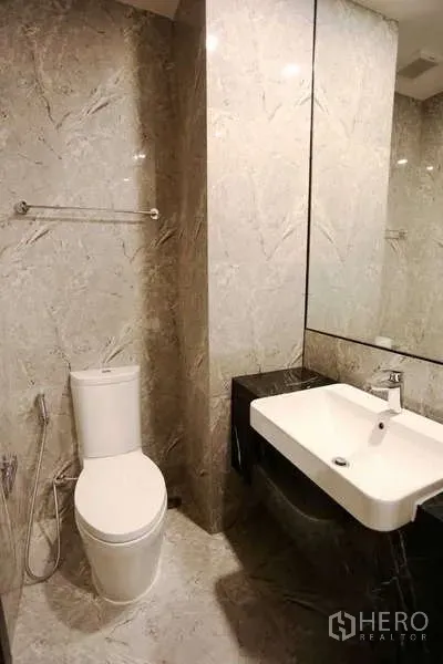 Condominium for rent in Watthana, Bangkok - Modern bathroom with large mirror, white basin and toilet, marble walls and bidet spray.