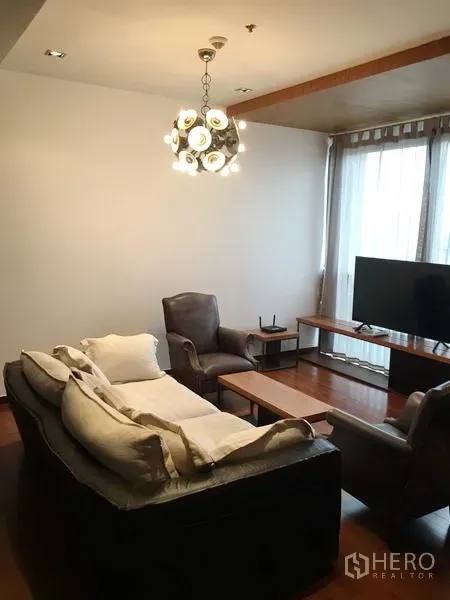 公寓 出租或出售在Khlong Toei, Bangkok - คลองเตย公寓客厅，配皮沙发、单人椅、电视与现代吊灯。