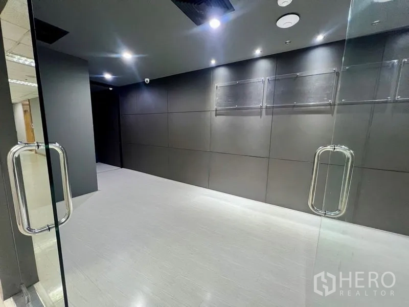 Office Space for rent in Watthana, Bangkok - Glass double-door entry to modern office lobby with dark feature wall and spotlights.