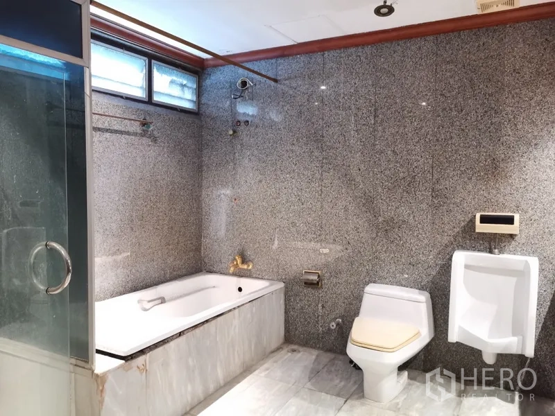 Condominium for sale in Watthana, Bangkok - Granite-clad bathroom with bathtub, glass shower, toilet and urinal.