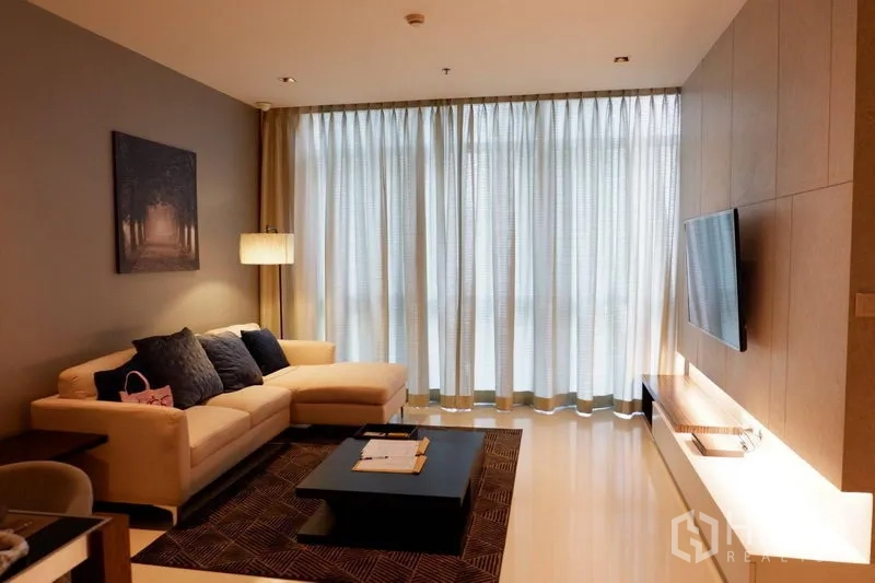 Condominium for rent in Pathum Wan, Bangkok - Pathum Wan condo living room with L-shaped sofa, sheer floor-to-ceiling curtains and wall-mounted TV.