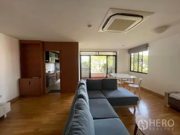 Condominium for rent in Watthana, Bangkok - Bright living room with L-shaped sofa, wood floors, dining area and balcony in an Ekkamai condo.