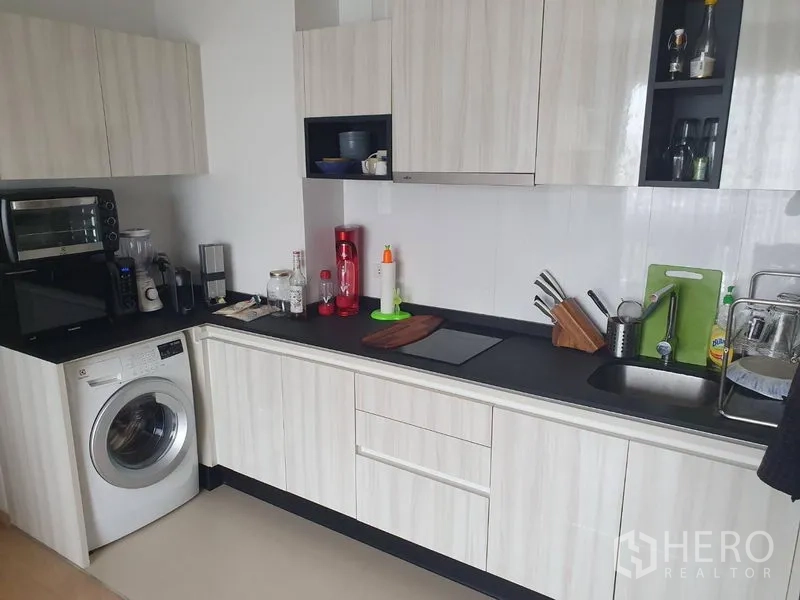 公寓 出租在Watthana, Bangkok - 走廊式厨房，浅木橱柜、黑色台面、水槽与洗衣机