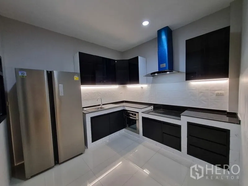 Detached House for rent in Bang Khae, Bangkok - Modern L-shaped kitchen with black cabinetry, stainless fridge, and range hood.