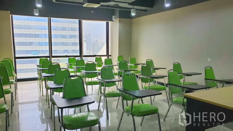 办公空间 出租在Watthana, Bangkok - 培训教室，多排绿色带写字板椅子，窗外城市景观。