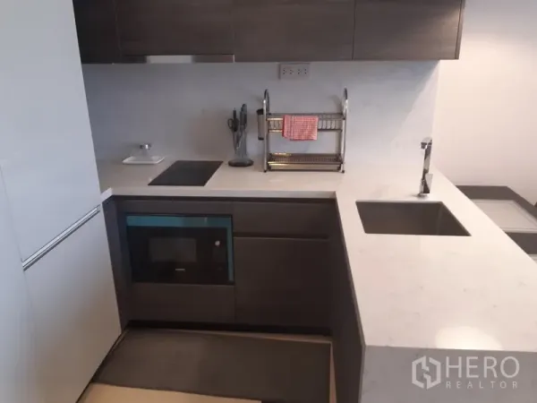 Condominium for rent or sale in Watthana, Bangkok - Modern L-shaped kitchen with white quartz countertops, grey cabinetry, induction hob and built-in oven.
