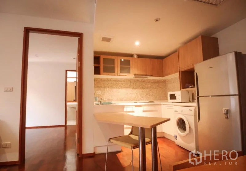 Condominium for rent in Pathum Wan, Bangkok - L-shaped kitchen with mosaic backsplash, breakfast bar, fridge and washer, opening toward the bedroom and bathroom.