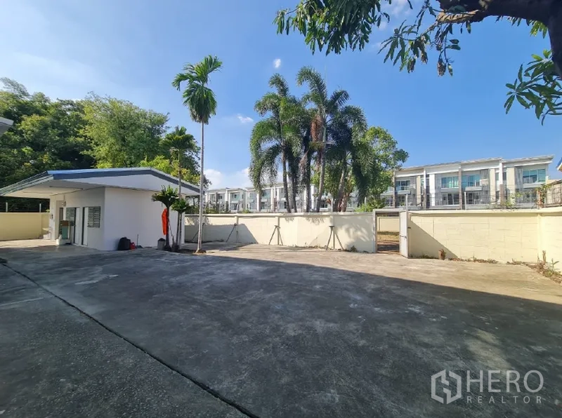 Warehouse for rent in Khlong Toei, Bangkok - Rear yard with a small utility building, palm trees and nearby residences.