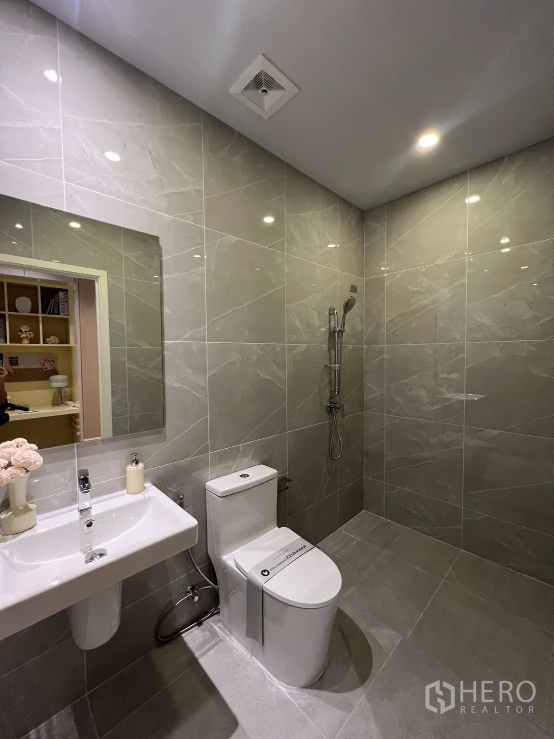 Townhouse for rent in Mueang Samut Prakan, Samut Prakan - Compact bathroom with sink, toilet, and handheld shower on glossy gray tiles.
