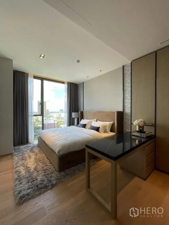 Condominium for rent or sale in Khlong Toei, Bangkok - Sunlit bedroom with floor-to-ceiling window, city view, plush rug, and built-in desk.