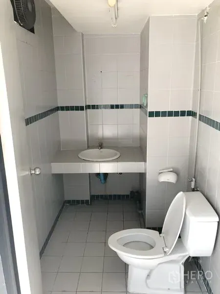 零售空间 出租在Khlong Toei, Bangkok - 紧凑卫生间，配有坐便器、洗手盆、瓷砖墙面与排风扇。