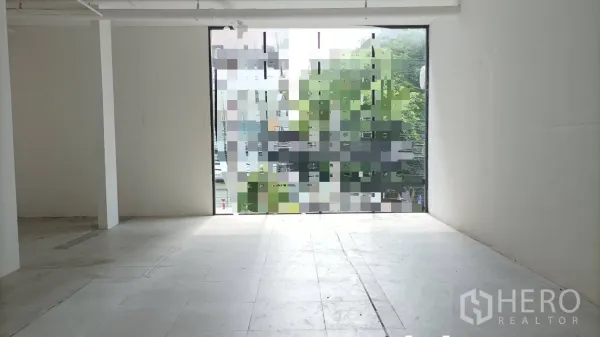 Retail Space for rent in Bangkok - Empty retail unit with tiled floor, central column, and large window facade overlooking greenery.