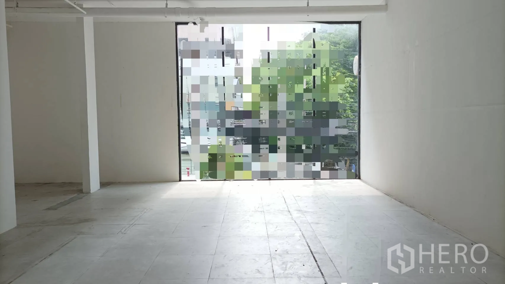 Retail Space for rent in Bangkok - Empty retail unit with tiled floor, central column, and large window facade overlooking greenery.