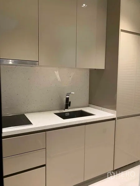 Condominium for rent in Watthana, Bangkok - Minimalist kitchenette with white countertop, sink and induction cooktop.